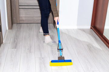 A woman washes the laminate floor in the apartment with a mop. House cleaning.