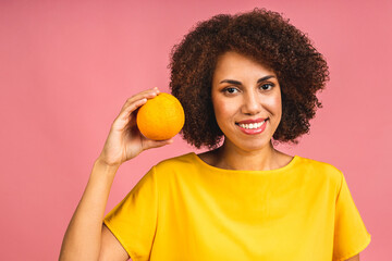 Lifestyle, food, diet and people concept: Photo of young cheerful african american woman holding orange fruit isolated on pink color background.