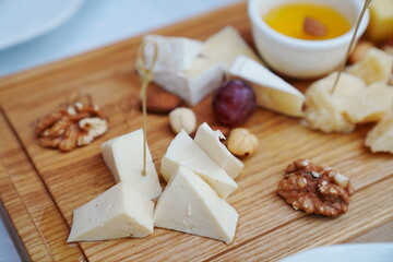 wooden tray with cheese cuts, nuts, grapes and honey. 