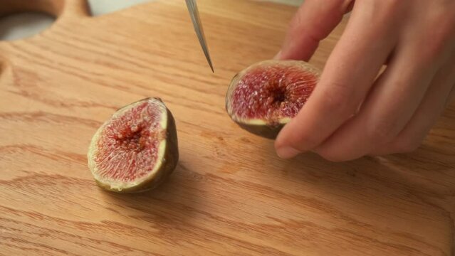 fresh cut figs close up. View of cutting fig fruit with knife. the girl cuts figs. women's hand cut ripe figs with a knife on a wooden board. women's hands spread sliced figs on a plate