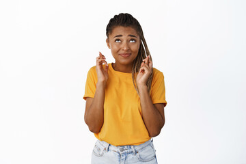 Cute nervous Black girl, student wishing, looking up with fingers crossed, praying, standing over white background