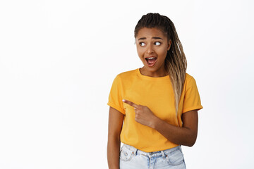 Surprised Black woman pointing and looking left, showing advertisement, being amazed by promo...