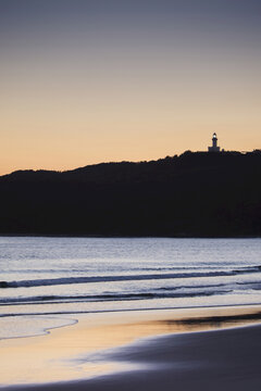 Silhouette of Cape Byron Lighthouse on hilltop and beach at sunset at Byron Bay in New South Wales, Australia