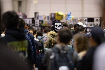 A male cosplayer in a military uniform and skull mask stands in the middle of a crowd of other...