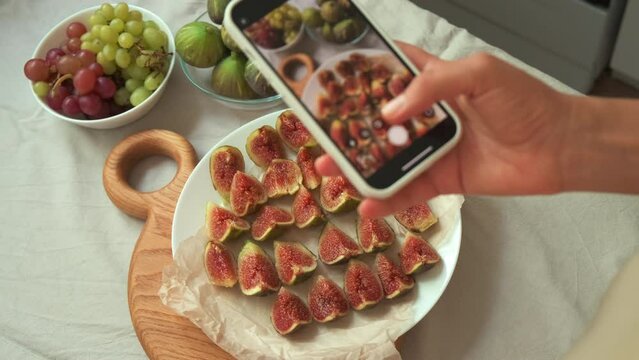 fresh cut figs close up. View of cutting fig fruit with knife. the girl cuts figs. a girl takes pictures of sliced figs on the table. a girl takes pictures of snacks on the table