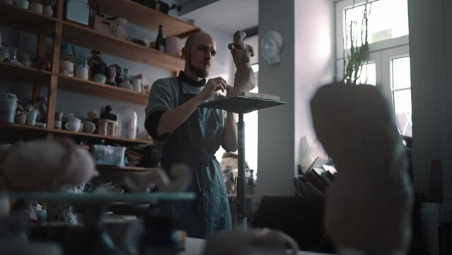 Full-length portrait of a skillful man potter creating a clay statue in his author's art workshop