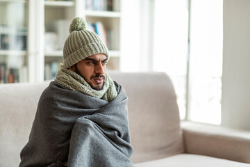 Freezing middle eastern guy sitting on couch in living room
