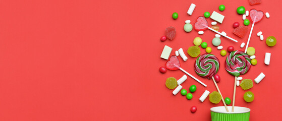 Cup and many tasty candies on red background with space for text