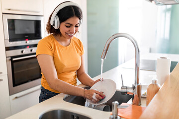 Smiling Arab Housewife Washing Dishes In Kitchen And Listening Music In Headphones