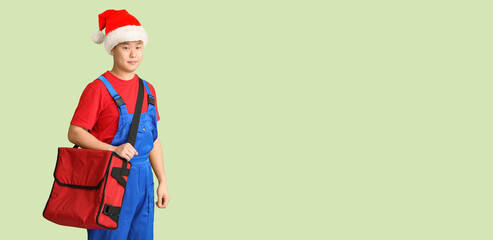 Asian courier of food delivery service in Santa hat on color background with space for text