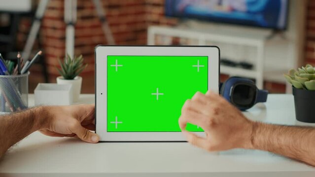 Male freelancer looking at horizontal greenscreen on display, working with wireless tablet at desk. Using isolated chroma key template and blank copy space with mock up on device. Close up.