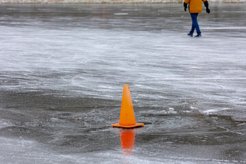 Orange traffic cone in the lake or river in winter during water turned to ice, To warning peoples...