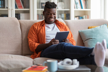 Smiling african american guy using digital pad at home