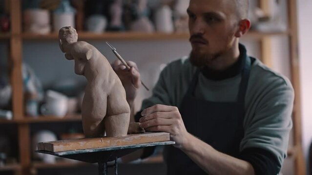 Skilled potter sculptor carefully working on a clay female statue with pottery loop in crafts studio