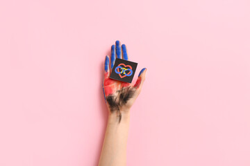 Painted female hand and paper with symbols of polyamory on pink background