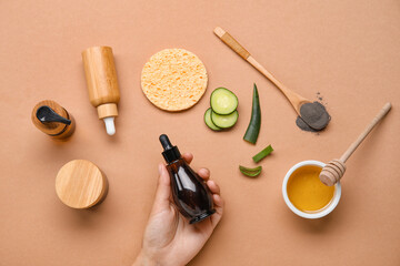 Female hand with bottles of cosmetic products and natural ingredients on color background