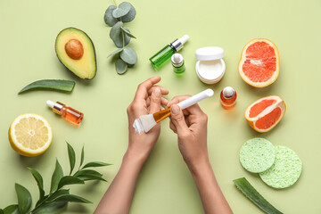 Female hands with cream and natural ingredients on green background