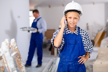 Portrait of preteen boy having phone conversation in house being renovating, his father painting wall on background