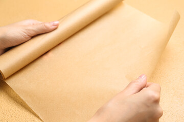 Female hands with baking paper on beige background, closeup