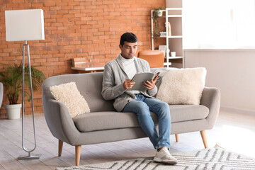 Fototapeta premium Young man reading magazine on grey sofa at home
