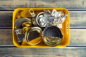 Yellow plastic box with metal canned caps, foil waste on wooden table background. Ecological...