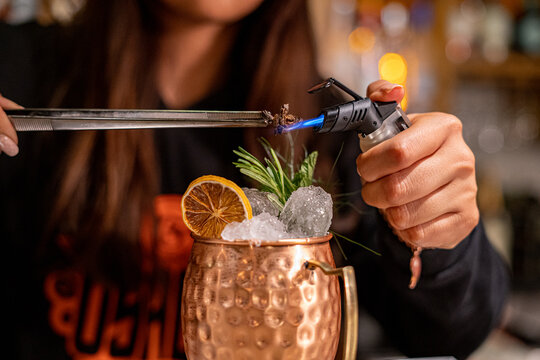 Making a moscow mule cocktail in a copper mug in a bar at night by a bartender, with a dried lemon garnish