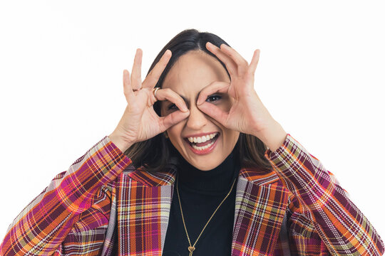 Young adult latin american woman facing camera laughing looking through fingers around her eyes. Pretend glasses. White background copy space horizontal portrait shot. High quality photo