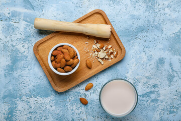 Glass of almond milk, wooden board with nuts and masher on color background