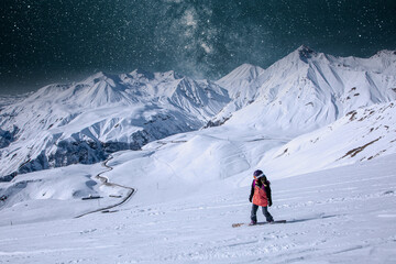 Fototapeta na wymiar night snowboarder girl is riding on snowboard under the starry sky in a big snowy mountains