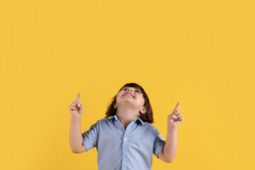 Cute little boy looking upward and pointing with both hands, enjoying interesting promo, orange background, empty space