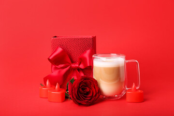 Glass cup of latte, candles, gift and rose on red background. Valentine's Day celebration