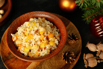 Board with bowl of rice Kutya and fir cones on dark table, closeup