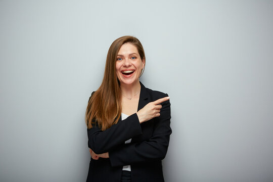 Smiling business woman in black suit pointing finger at side, isolated portrait.