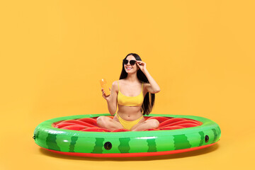 Happy young woman with sunscreen bottle on inflatable mattress against orange background. Seasonal suntan