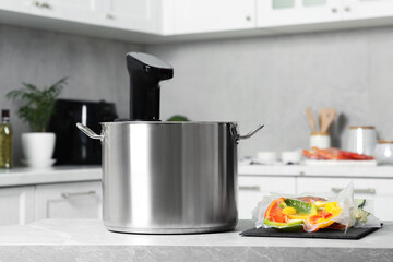 Pot with sous vide cooker and vacuum packed food products on table in kitchen. Thermal immersion circulator