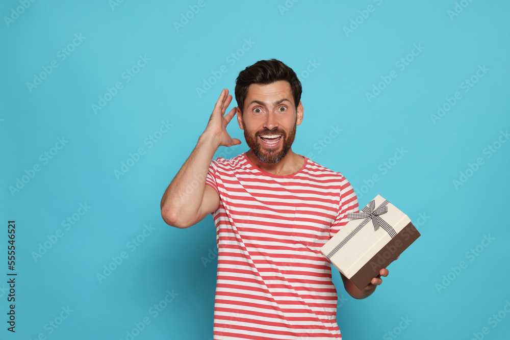 Wall mural Emotional man holding gift box on turquoise background