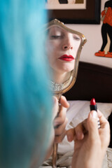 woman with blue hair applying lipstick with antique mirror