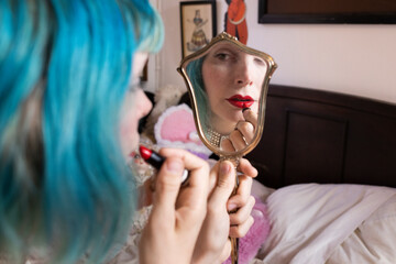 woman with blue hair applying lipstick with antique mirror