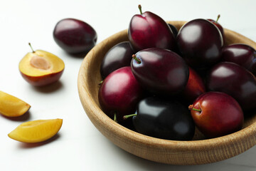Bowl with tasty ripe plums on white table, closeup