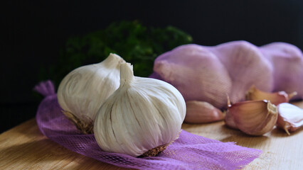 Cabezas de ajo sobre tela de color morado, cabezas de ajo envueltas en tela y dientes de ajo sobre una tabla de madera en fondo oscuro. Darckfood	