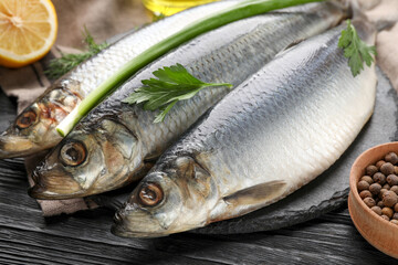 Delicious salted herrings and ingredients on black wooden table, closeup