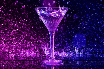 Glass of martini and splashes in neon lights on dark blue background, bokeh effect
