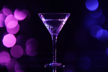 Glass of martini in neon lights on dark background, bokeh effect