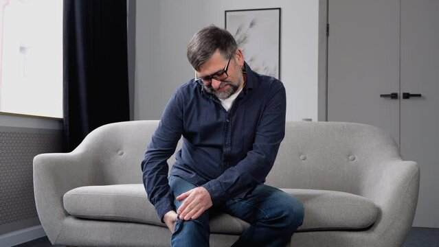 Uhappy senior man suffering from knee ache at home. Knee joint injury. Gout. Rheumatoid. Arthritis. Osteoporosis. Health care and problem concept