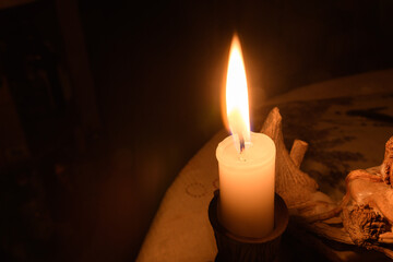 Macro photo of a burning white wax candle in a candlestick on a table in a room without light