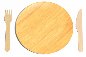 A biodegradable wooden plate in the middle of a wooden fork and knife on a white background