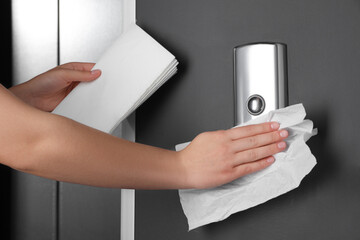 Woman cleaning elevator button with paper towel indoors, closeup