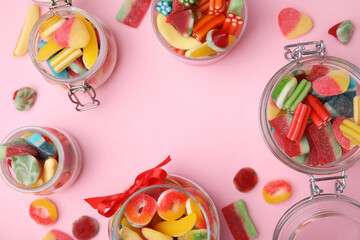 Frame made of glass jars with tasty colorful jelly candies on pink background, flat lay. Space for text