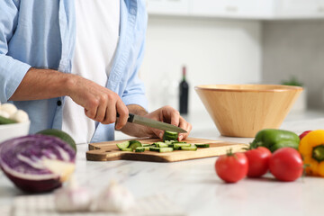 Man cutting cucumber at table in kitchen, closeup. Online cooking course