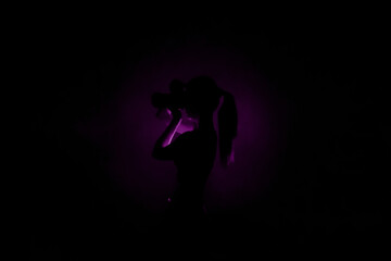 Center purple light silhouette on black background and lady photographer with camera taking photos. Concept of art photography. Dark violet  picture for website, avatar, Surreal abstract backdrop